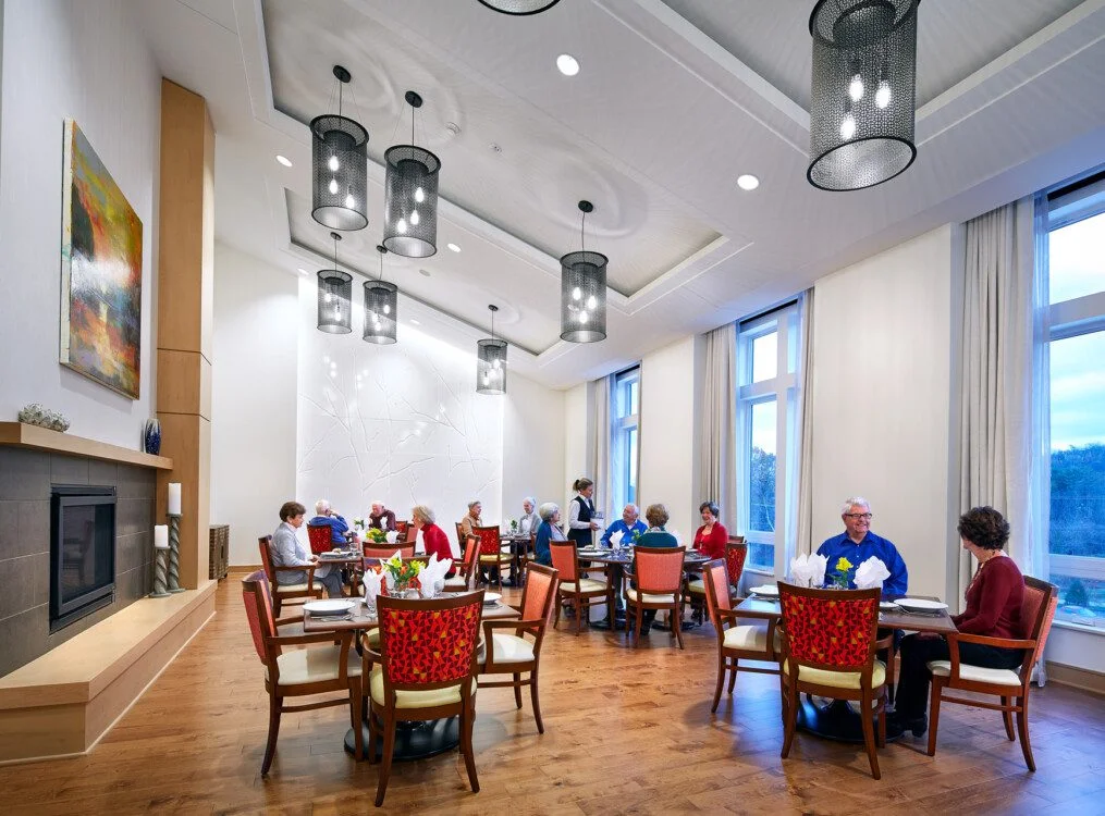Elegant dining room with people seated at tables, large windows, and modern lighting.