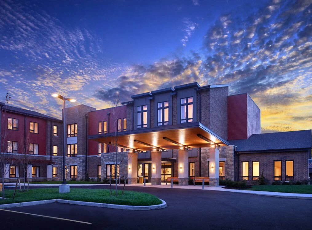 Modern building entrance at dusk with illuminated windows and vibrant sky.
