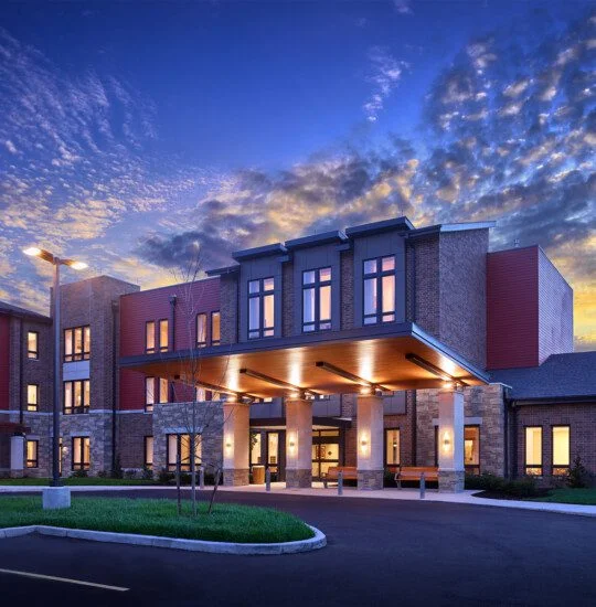 Modern building entrance at dusk with illuminated windows and vibrant sky.