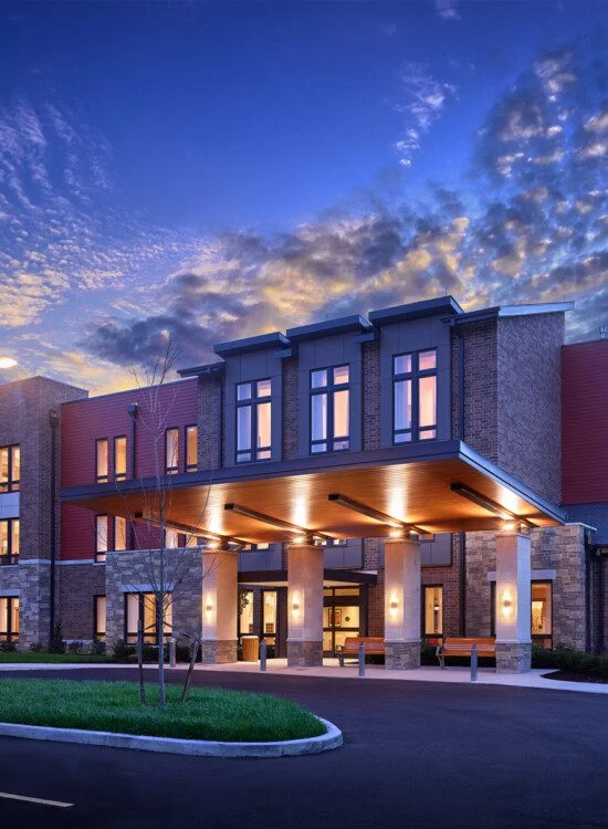 Modern building entrance at dusk with illuminated windows and vibrant sky.