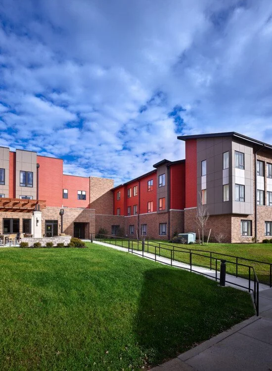 Modern multi-story building surrounded by grass, under a partly cloudy sky.
