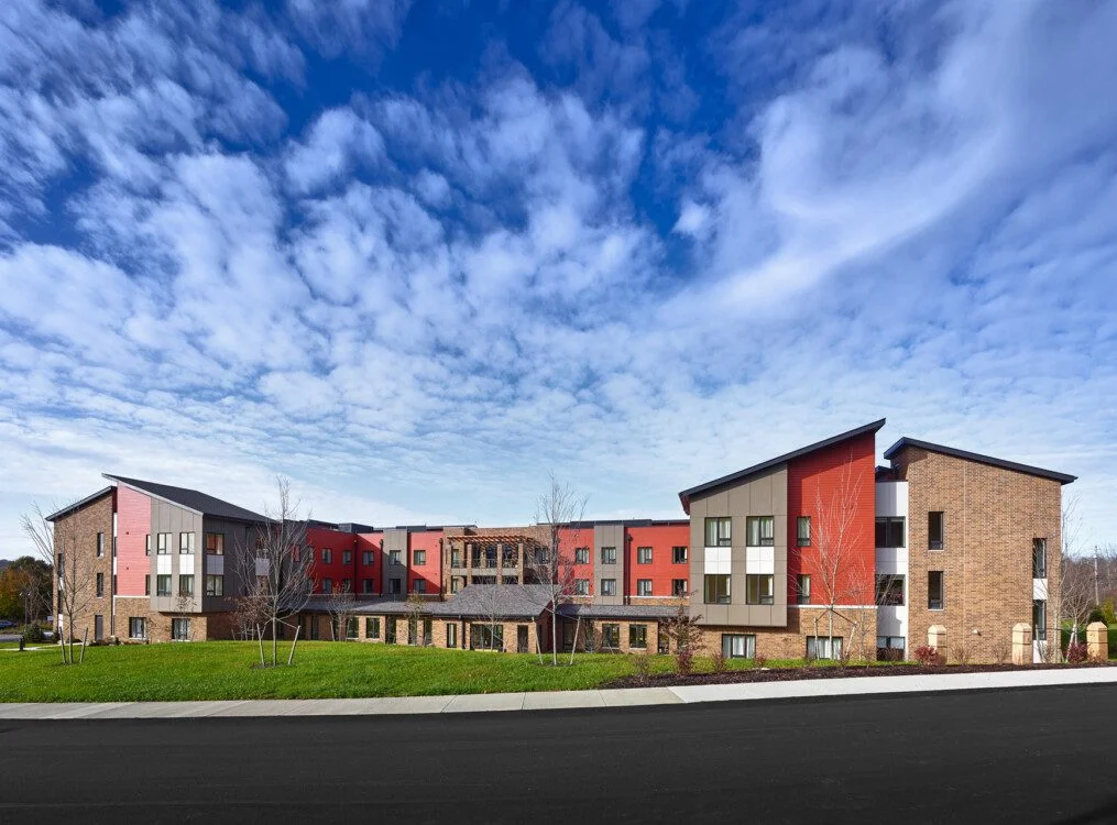 Modern building with red and beige exterior under a blue sky with scattered clouds.