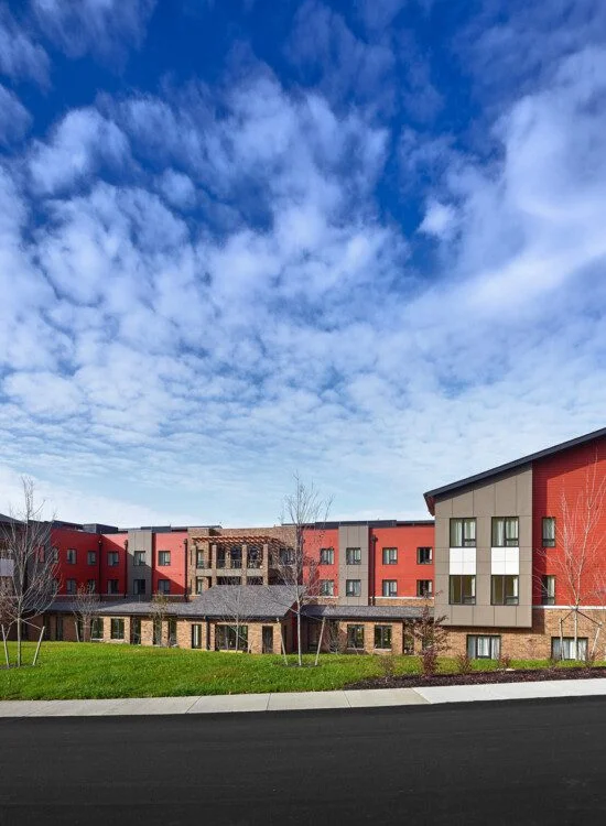 Modern building with red and beige exterior under a blue sky with scattered clouds.