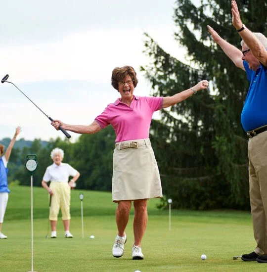 Seniors celebrating a successful putt on a golf course.