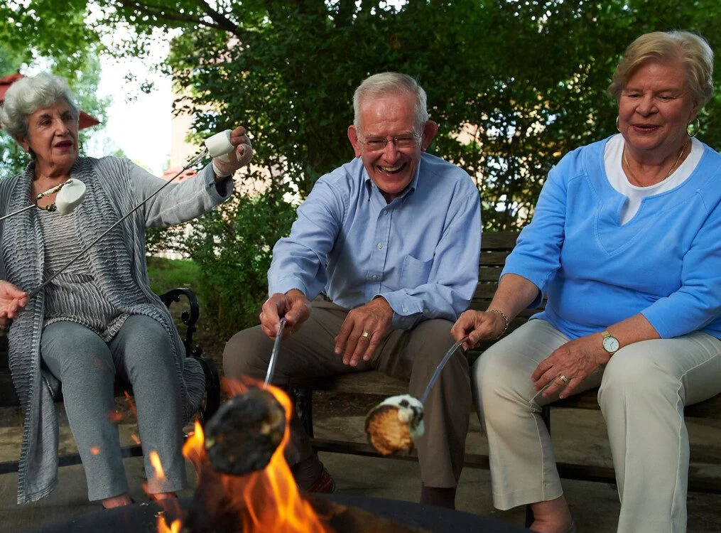 Seniors roasting marshmallows over a firepit, smiling and enjoying the outdoors.
