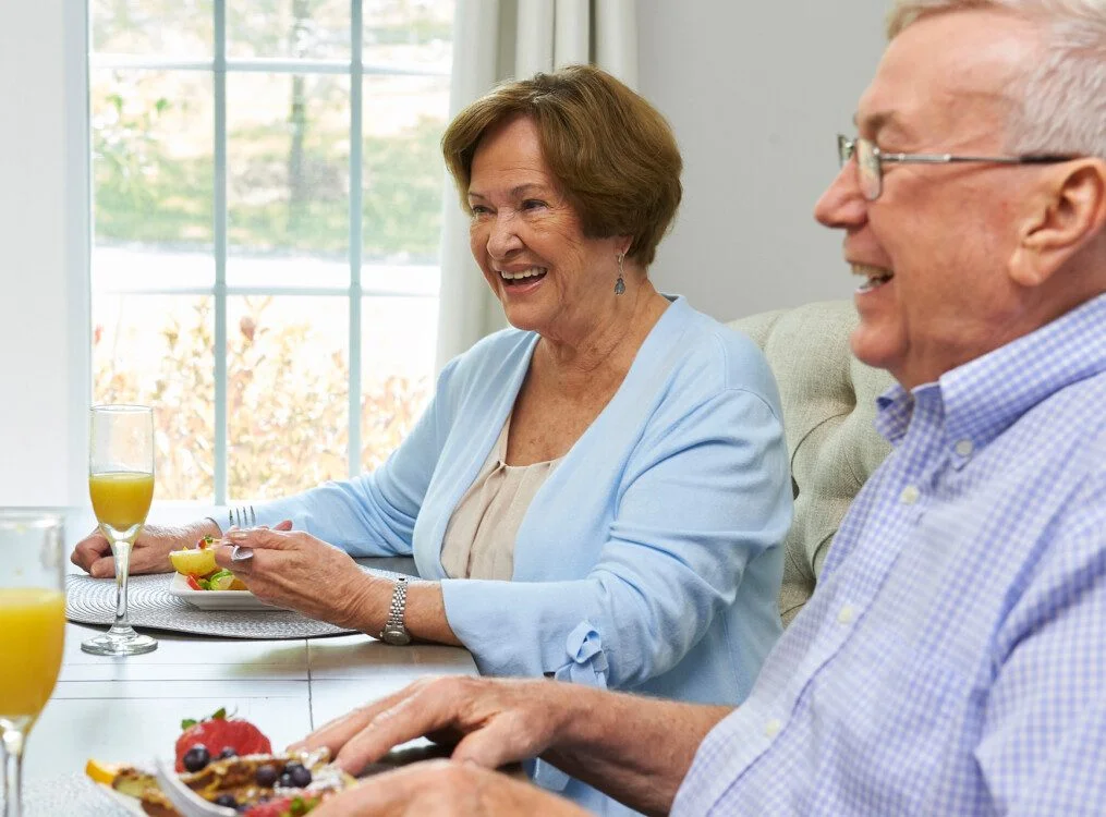 Elderly couple enjoying breakfast with orange juice at a dining table.