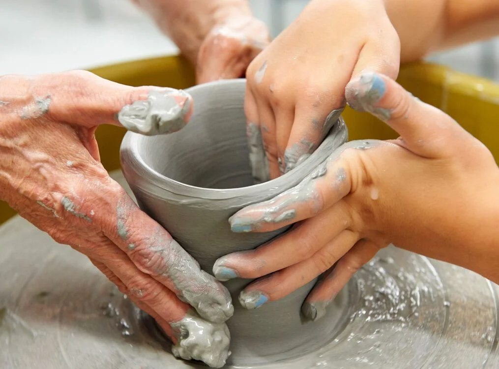 Hands shaping a clay pot on a pottery wheel.
