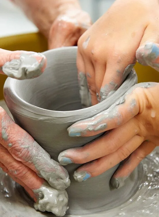 Hands shaping a clay pot on a pottery wheel.