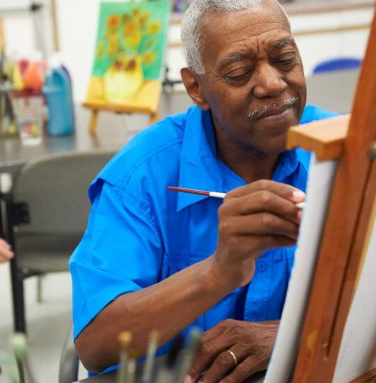 Man in blue shirt painting on canvas in art studio.