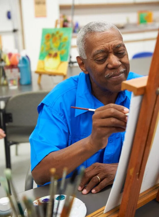 Man in blue shirt painting on canvas in art studio.