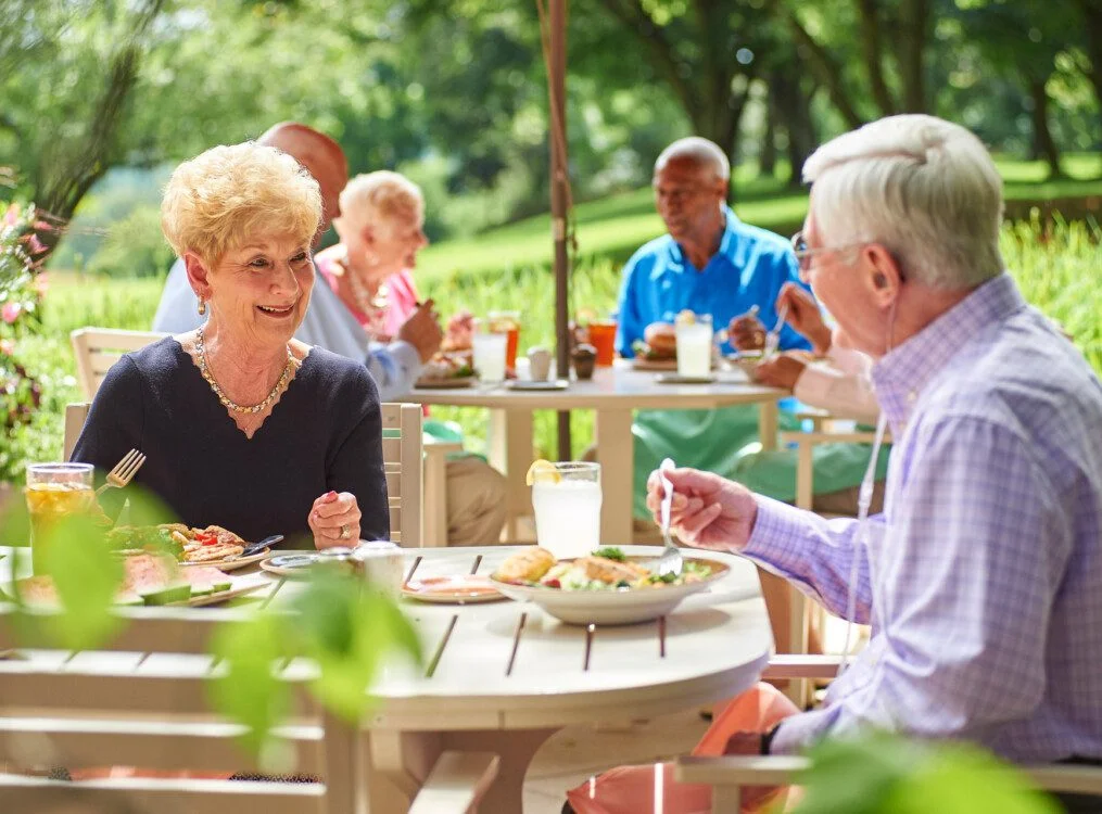Seniors enjoying a meal together outdoors at a garden patio on a sunny day.