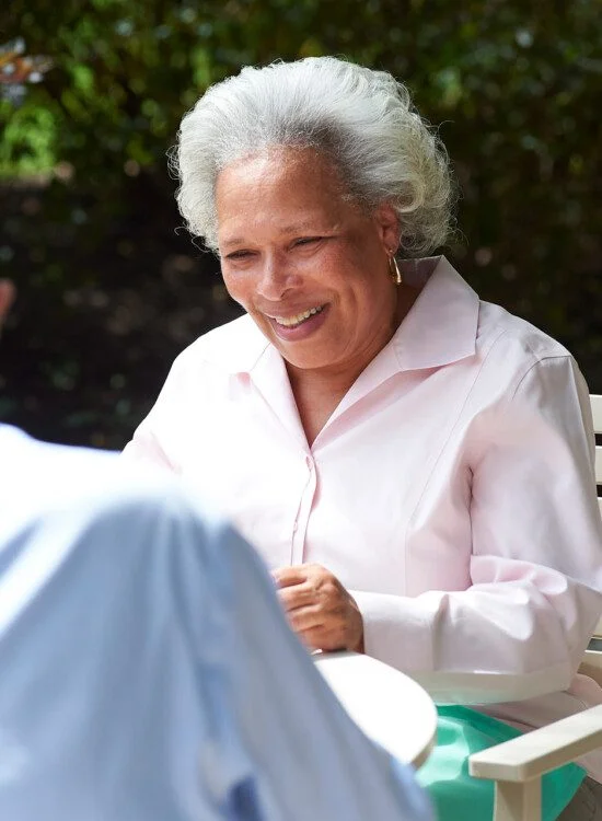 Elderly woman smiling in conversation with a man outdoors.