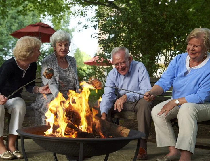 Four seniors roasting marshmallows over a fire pit, smiling and enjoying the outdoors.