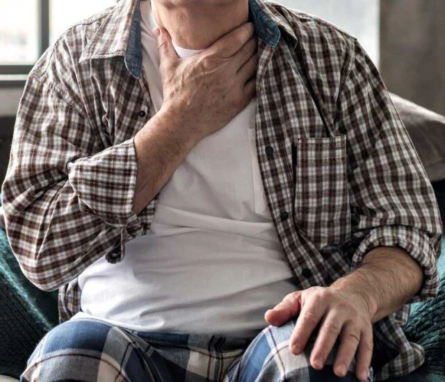 Person sitting and touching throat, appearing unwell.