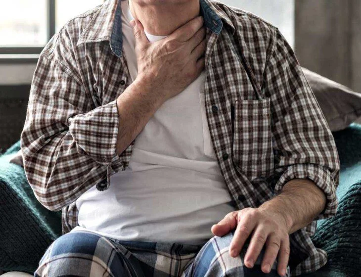 Person sitting and touching throat, appearing unwell.