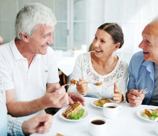 Four adults laughing and dining together at a table with coffee and pastries.