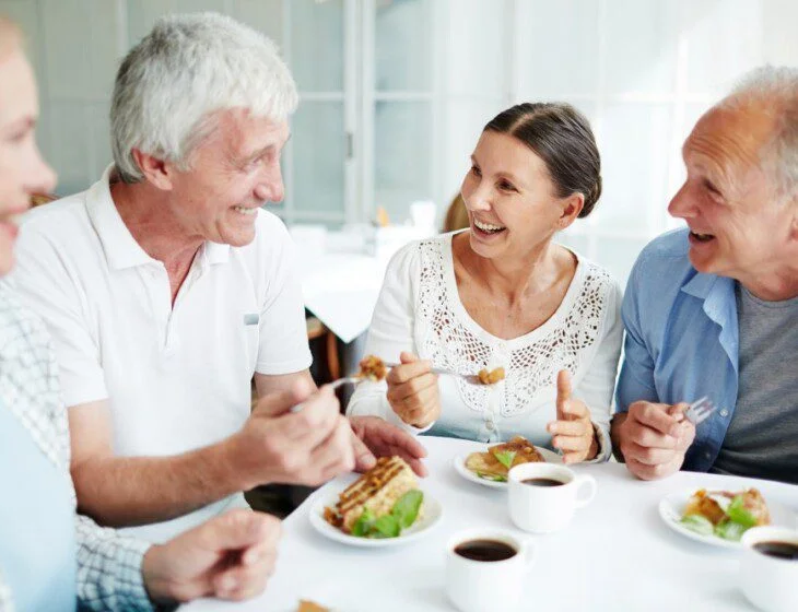 Four adults laughing and dining together at a table with coffee and pastries.