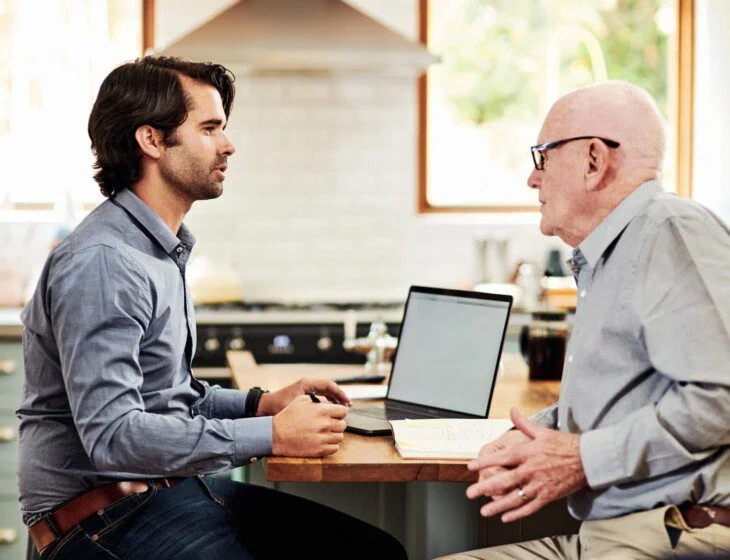 Two people having a discussion at a table with a laptop and papers.