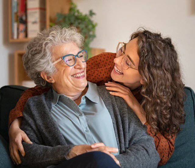 Elderly woman and younger woman smiling together on a couch.