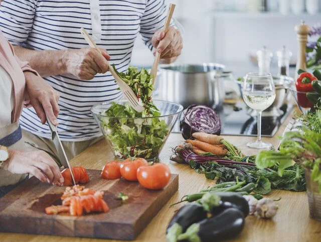Two people preparing a vegetable salad in a kitchen.