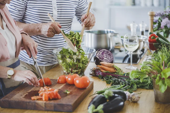 Two people preparing a vegetable salad in a kitchen.