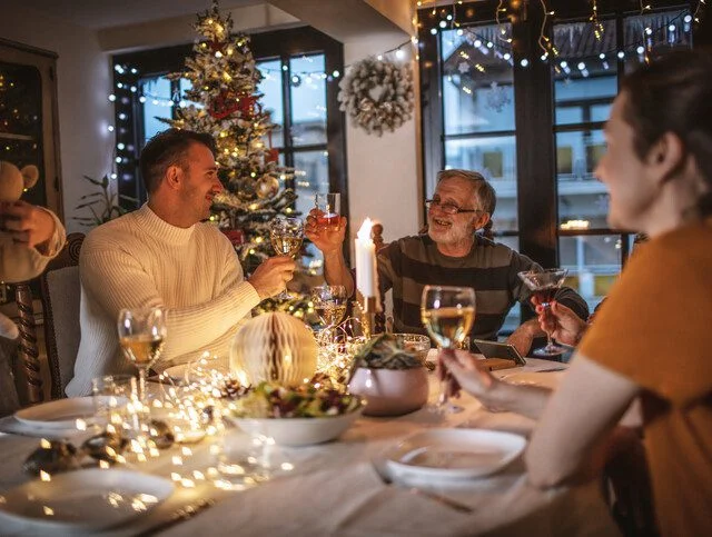 Family celebrating around a festive table with decorations and a Christmas tree.