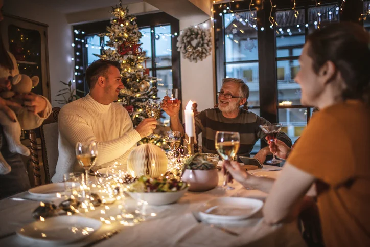 Family celebrating around a festive table with decorations and a Christmas tree.