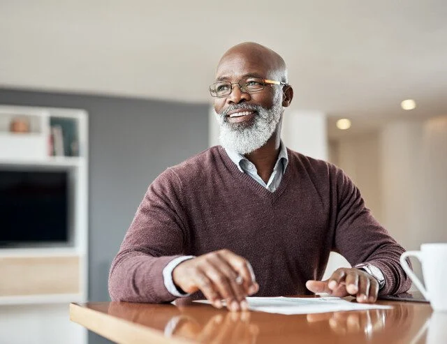 Smiling man sitting at a desk with papers and a mug.