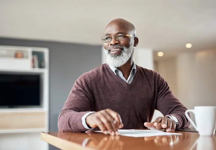 Smiling man sitting at a desk with papers and a mug.