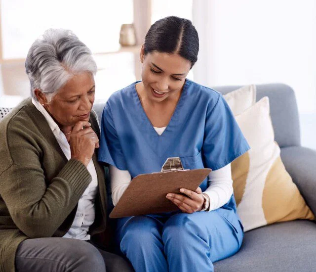 Nurse showing an elderly woman a clipboard while sitting on a sofa.