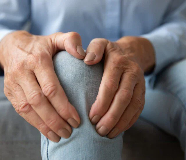 Hands holding a knee, wearing blue jeans.