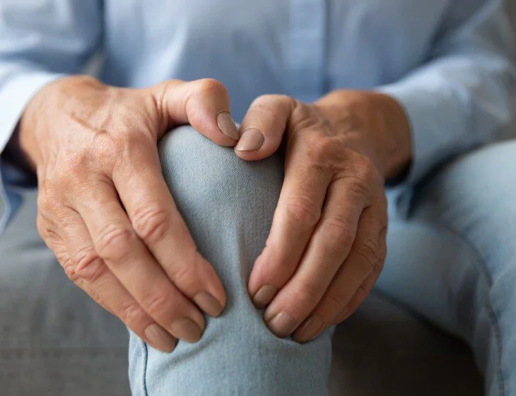Hands holding a knee, wearing blue jeans.