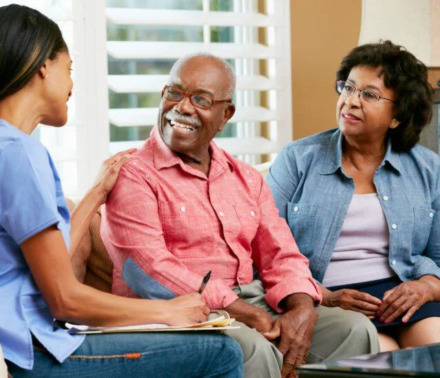 Caregiver talking with an elderly couple, smiling indoors.