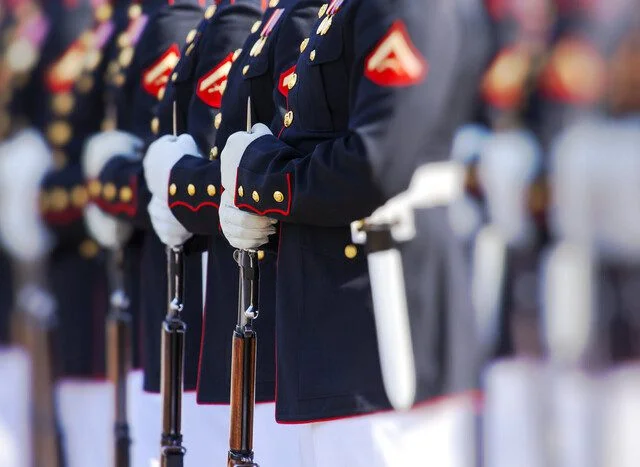 Military officers in uniform standing in formation, holding rifles.