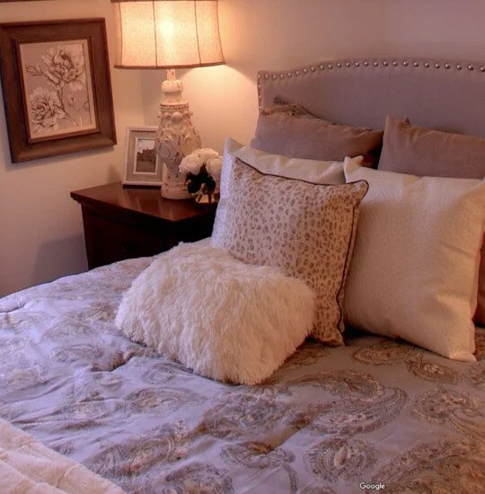 Cozy bedroom with patterned bedding, plush pillows, and a warm lamp on a side table.