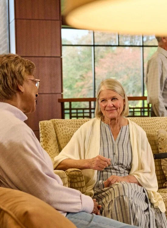 Two women seated on a couch in conversation, with two men chatting in the background.