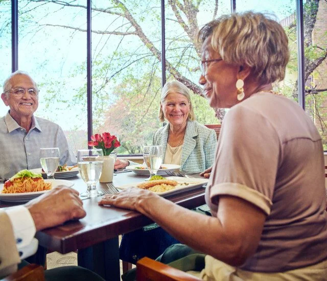 Seniors dining and smiling in a bright, windowed restaurant setting.