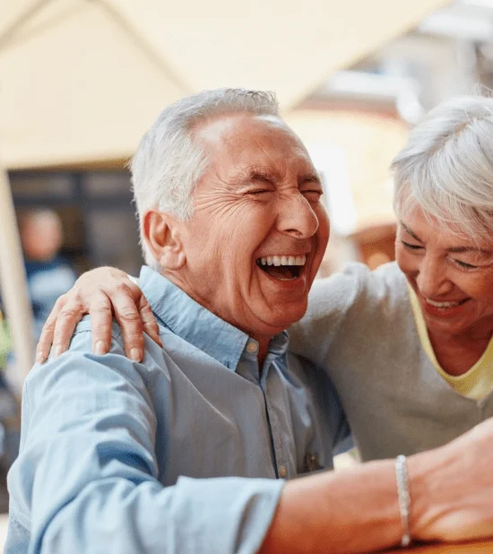 Elderly couple laughing and enjoying coffee outdoors under an umbrella.