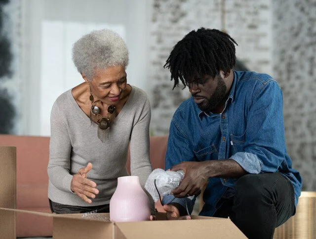 A young man of African descent and his mother have just moved into a new house and are unpacking a box together.