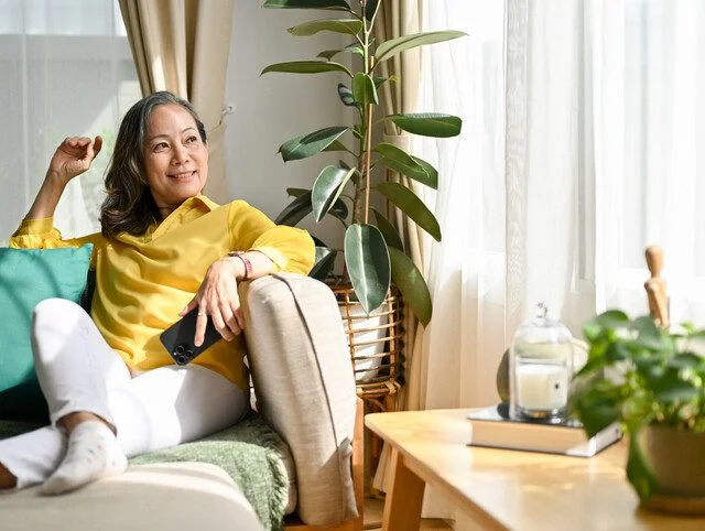 older adult woman smiling while sitting on the couch looking out the window
