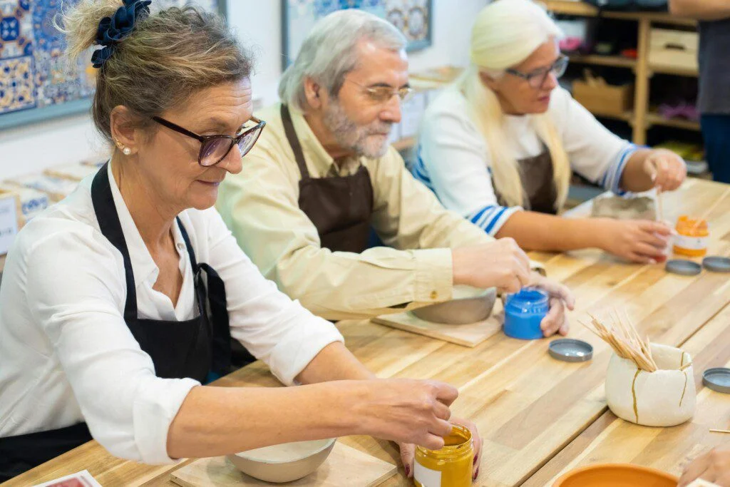 Three people painting pottery at a workshop table, focused and engaged in their work.