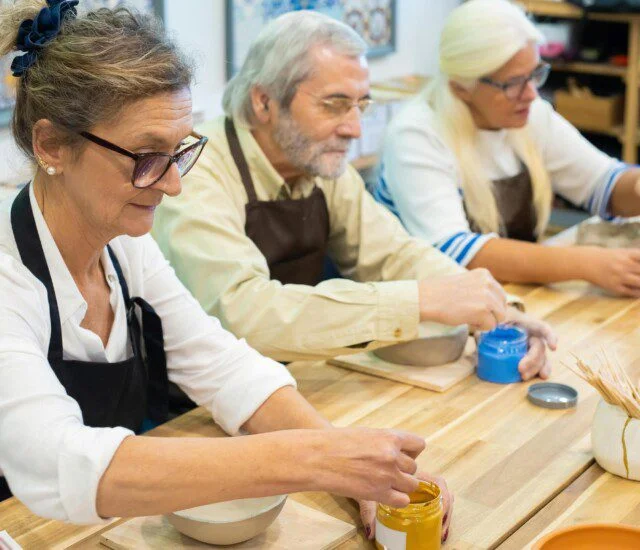 Three people painting pottery at a workshop table, focused and engaged in their work.