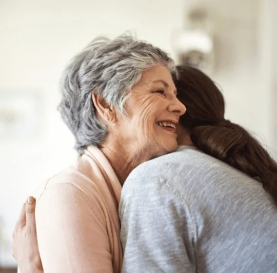 Older woman and younger woman hugging warmly indoors.