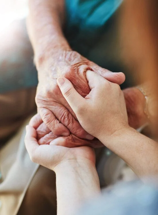 Young hands gently holding an elderly person's hands.