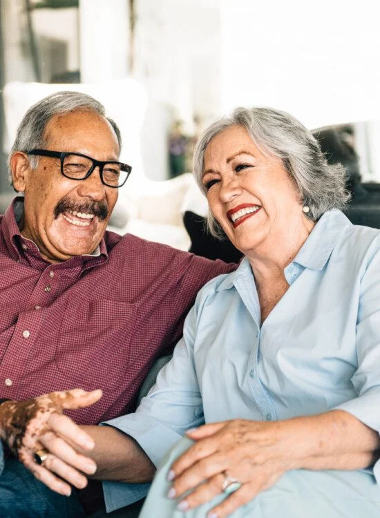 Older couple smiling and laughing while sitting together on a couch.