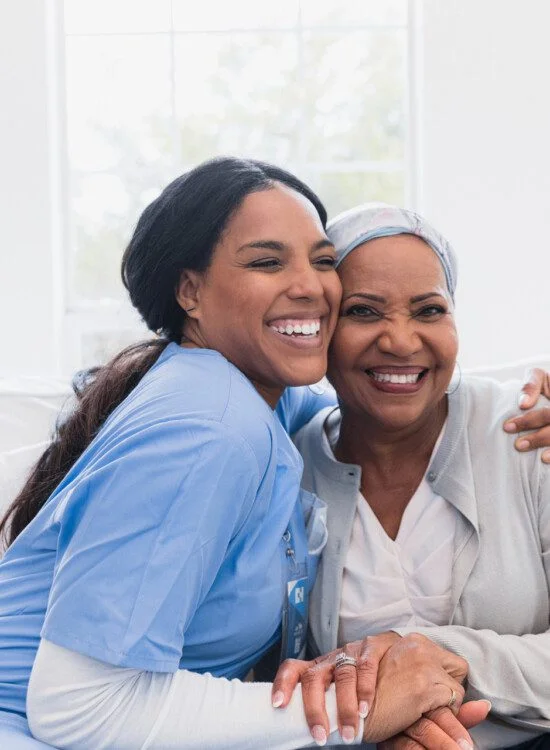 Nurse and elderly woman smiling and embracing in a bright room.