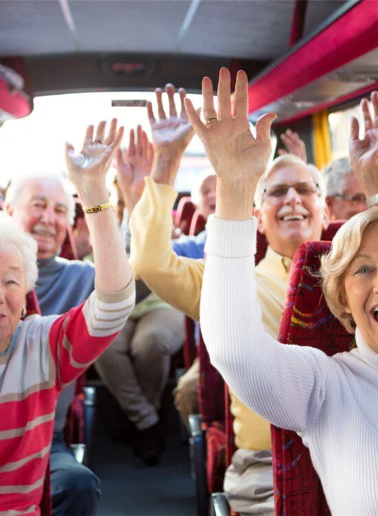 Elderly group smiling and raising hands on a bus.