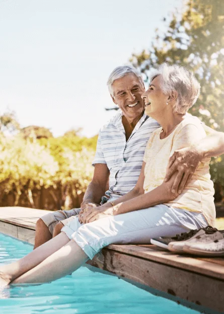 Older couple smiling by a pool in sunlight.