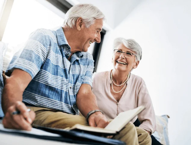 Elderly couple smiling and reading a book together at home.