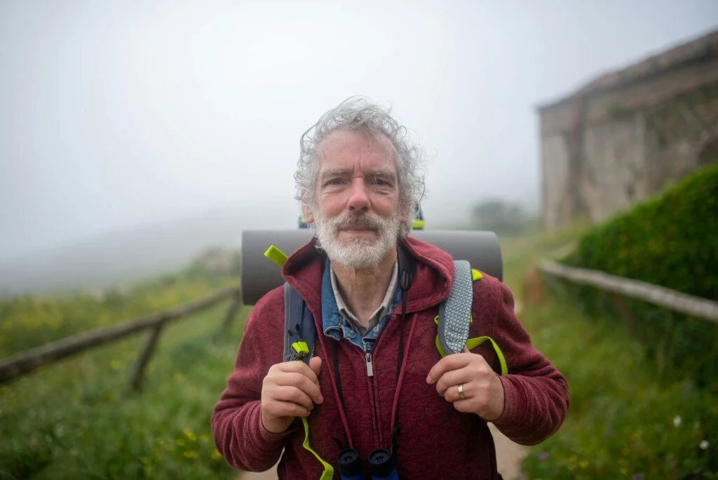 Man in a red jacket hiking outdoors on a foggy day.